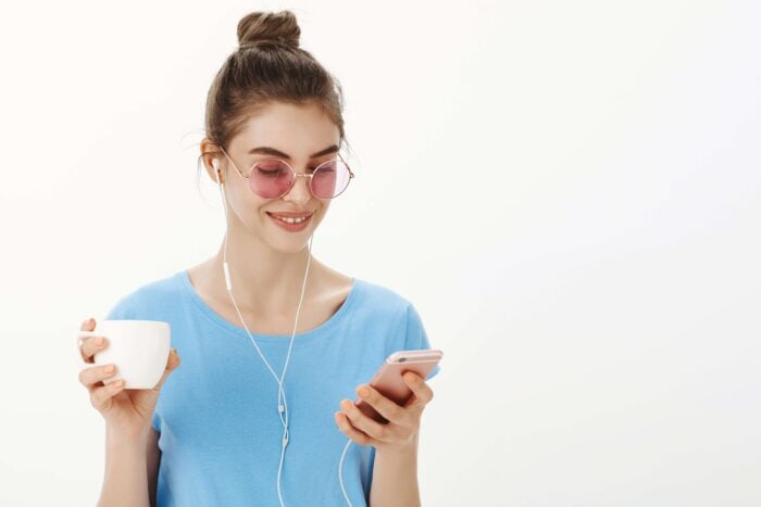 Young woman listening to Greek podcasts on her phone as she drinks coffee.