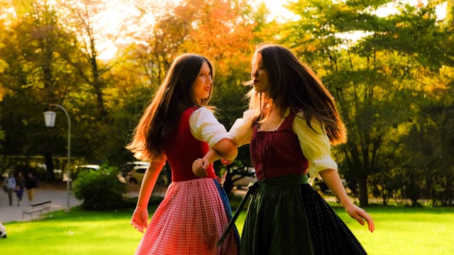 Two women in traditional dresses dancing outdoors.