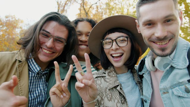 A diverse group of young adults smile outdoors while posing together for a selfie.