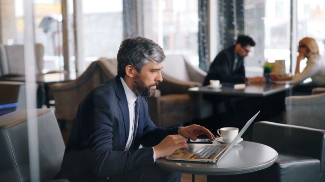 Business professional writing a formal email in German on a laptop in a café.